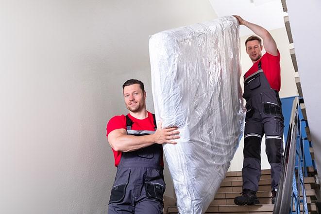 two people carrying a box spring out of a room in Holbrook